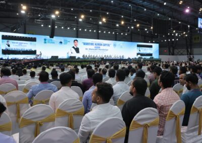 Ein großes Publikum sitzt in Reihen weißer Stühle mit goldenen Schleifen vor einer Bühne mit einem Bildschirm und Rednern auf einer Konferenz mit dem Titel Maritime Human Capital in einer geräumigen, gut beleuchteten Kongresshalle.