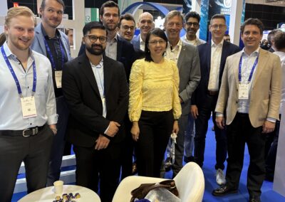 Eine Gruppe von Männern und Frauen steht in Business-Kleidung an einem Stand mit der Aufschrift "German Maritime Centre". Sie lächeln, tragen Schlüsselbänder um den Hals und befinden sich in einem professionellen Innenbereich.